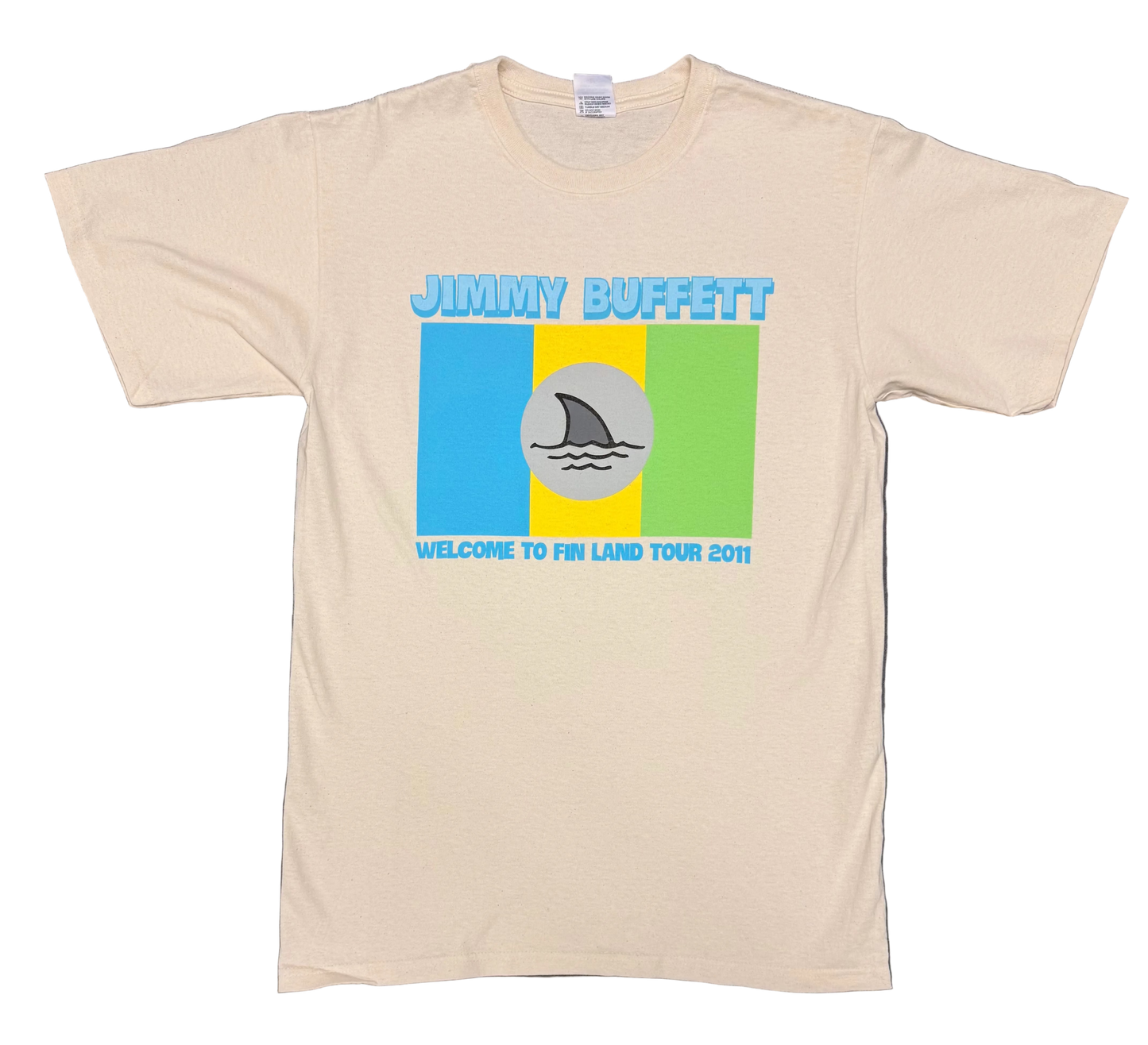Natural off white short sleeve Jimmy Buffett tee featuring bold blue “Jimmy Buffett” lettering above a retro blue, yellow, and green color block graphic. A gray circle with a shark fin cutting through waves appears at center, with “Welcome to Fin Land Tour 2011” printed below.