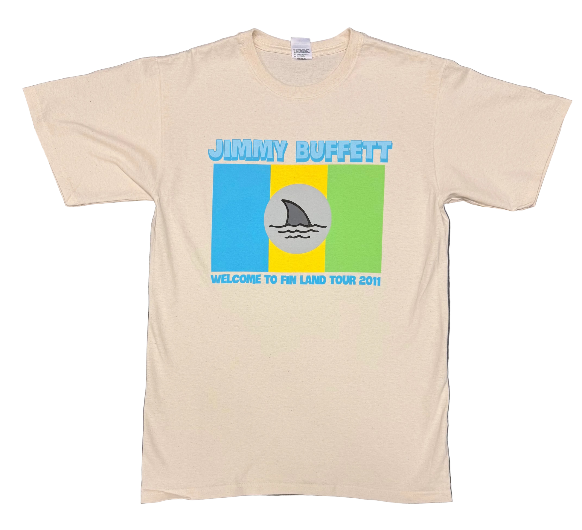 Natural off white short sleeve Jimmy Buffett tee featuring bold blue “Jimmy Buffett” lettering above a retro blue, yellow, and green color block graphic. A gray circle with a shark fin cutting through waves appears at center, with “Welcome to Fin Land Tour 2011” printed below.