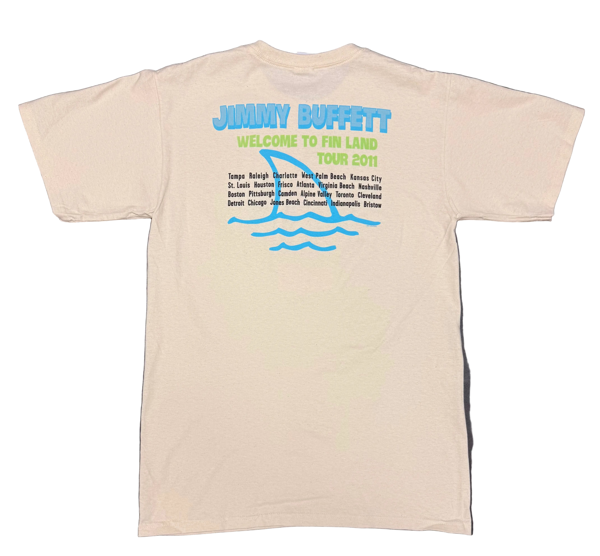 Back of a natural off white short sleeve Jimmy Buffett tee featuring large blue “Jimmy Buffett” lettering above green “Welcome to Fin Land Tour 2011” text. A large blue shark fin and wave graphic appears behind a list of tour cities printed in black.