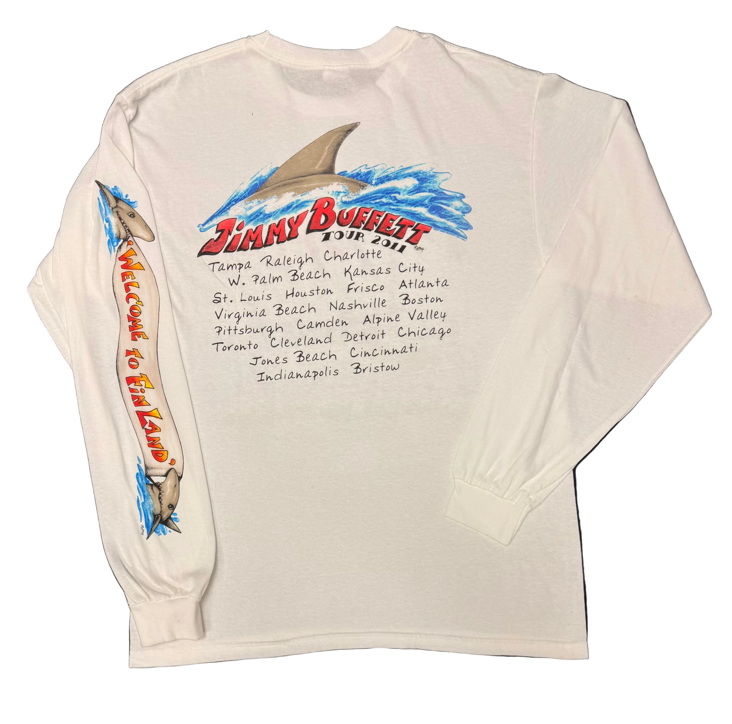 Back of a white long sleeve Jimmy Buffett tee featuring a large shark fin rising through blue waves above red “Jimmy Buffett Tour 2011” lettering and a handwritten style list of tour cities. The sleeve features shark graphics and vertical “Welcome to Fin Land” lettering.