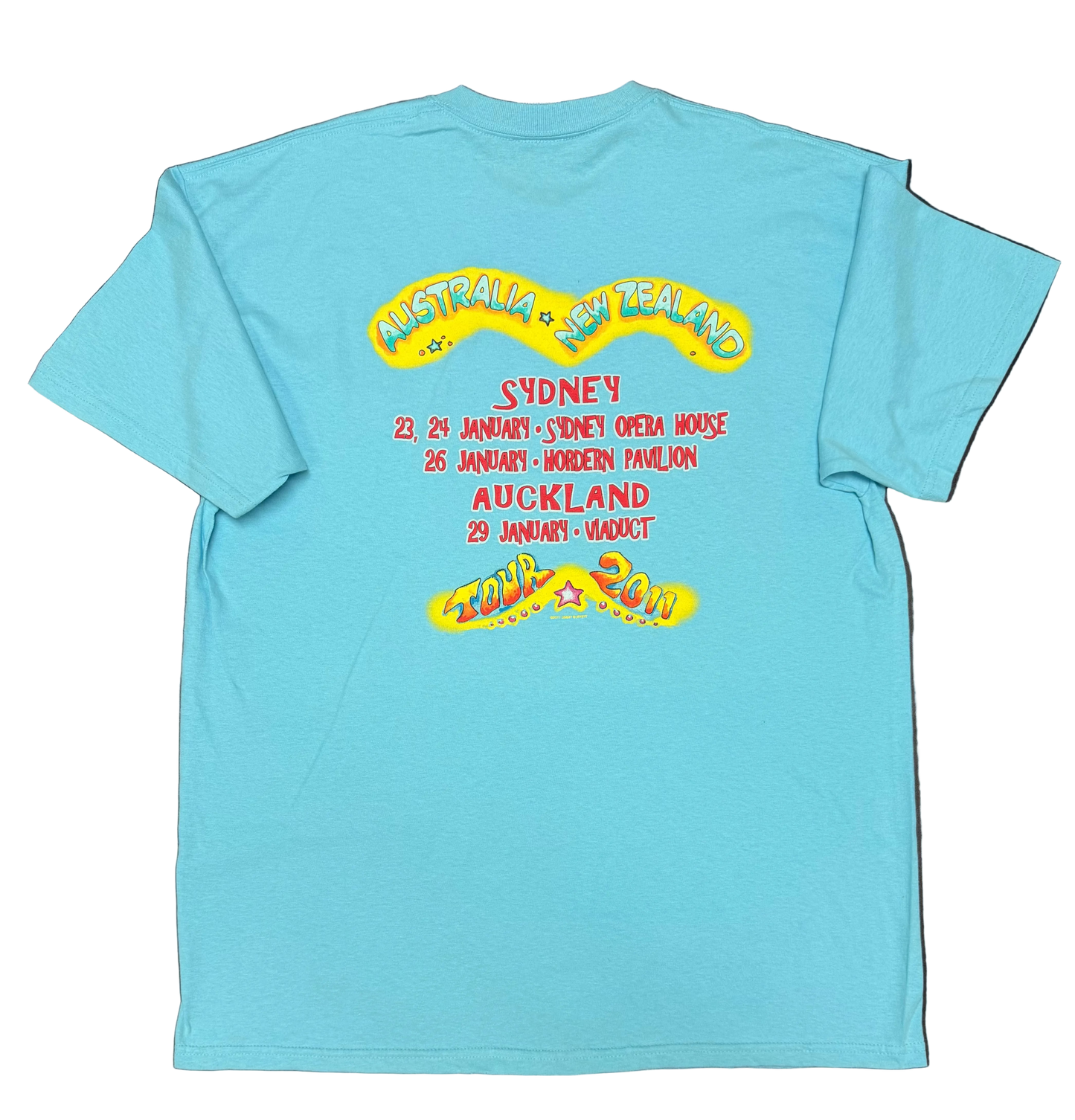 Back of an aqua blue short sleeve Jimmy Buffett tee featuring large “Australia + New Zealand” lettering above the 2011 tour dates. The design lists Sydney performances at the Sydney Opera House on January 23 and 24, Hordern Pavilion on January 26, and Auckland Viaduct on January 29, with colorful “Tour 2011” artwork at the bottom.