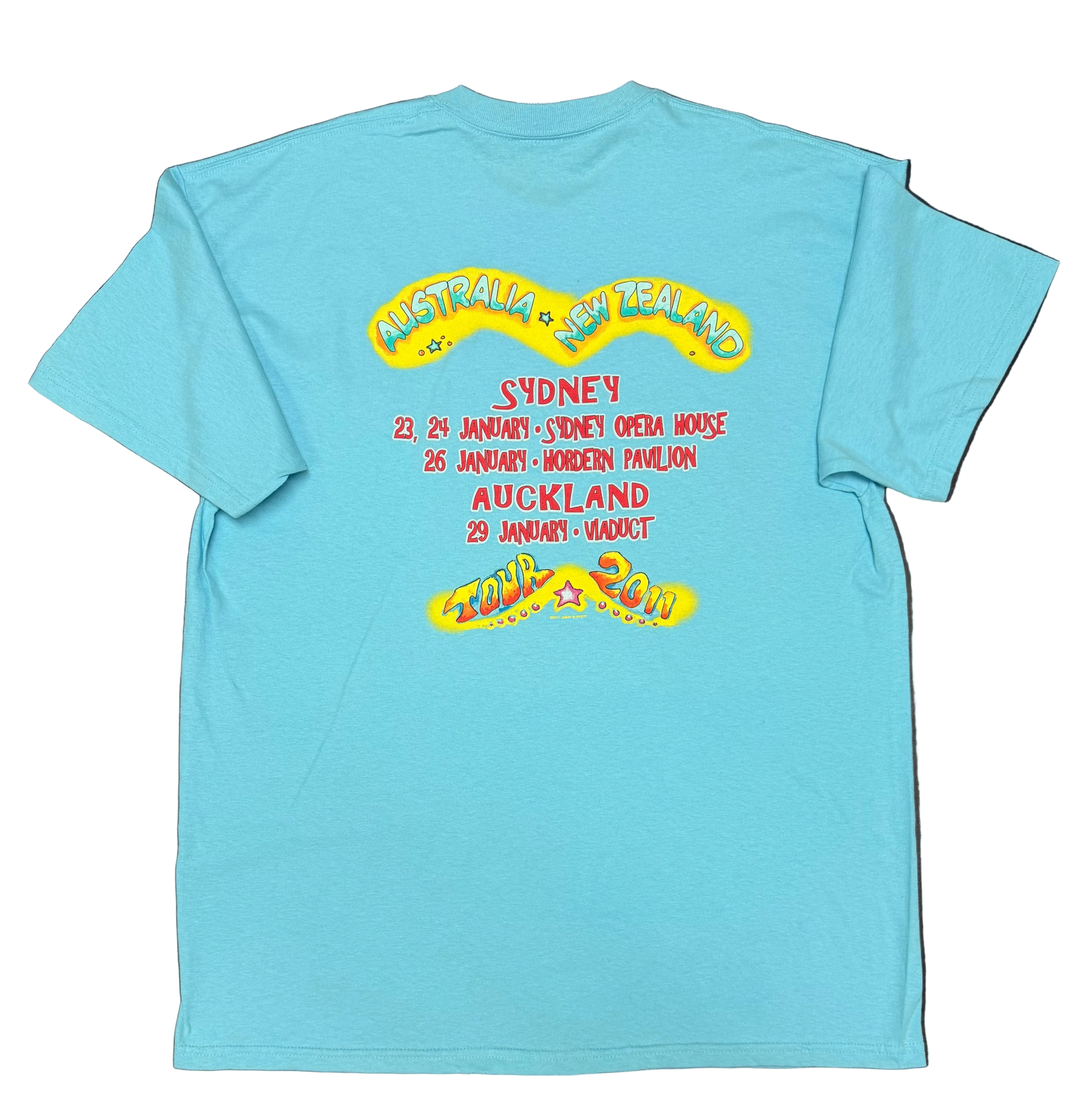 Back of an aqua blue short sleeve Jimmy Buffett tee featuring large “Australia + New Zealand” lettering above the 2011 tour dates. The design lists Sydney performances at the Sydney Opera House on January 23 and 24, Hordern Pavilion on January 26, and Auckland Viaduct on January 29, with colorful “Tour 2011” artwork at the bottom.