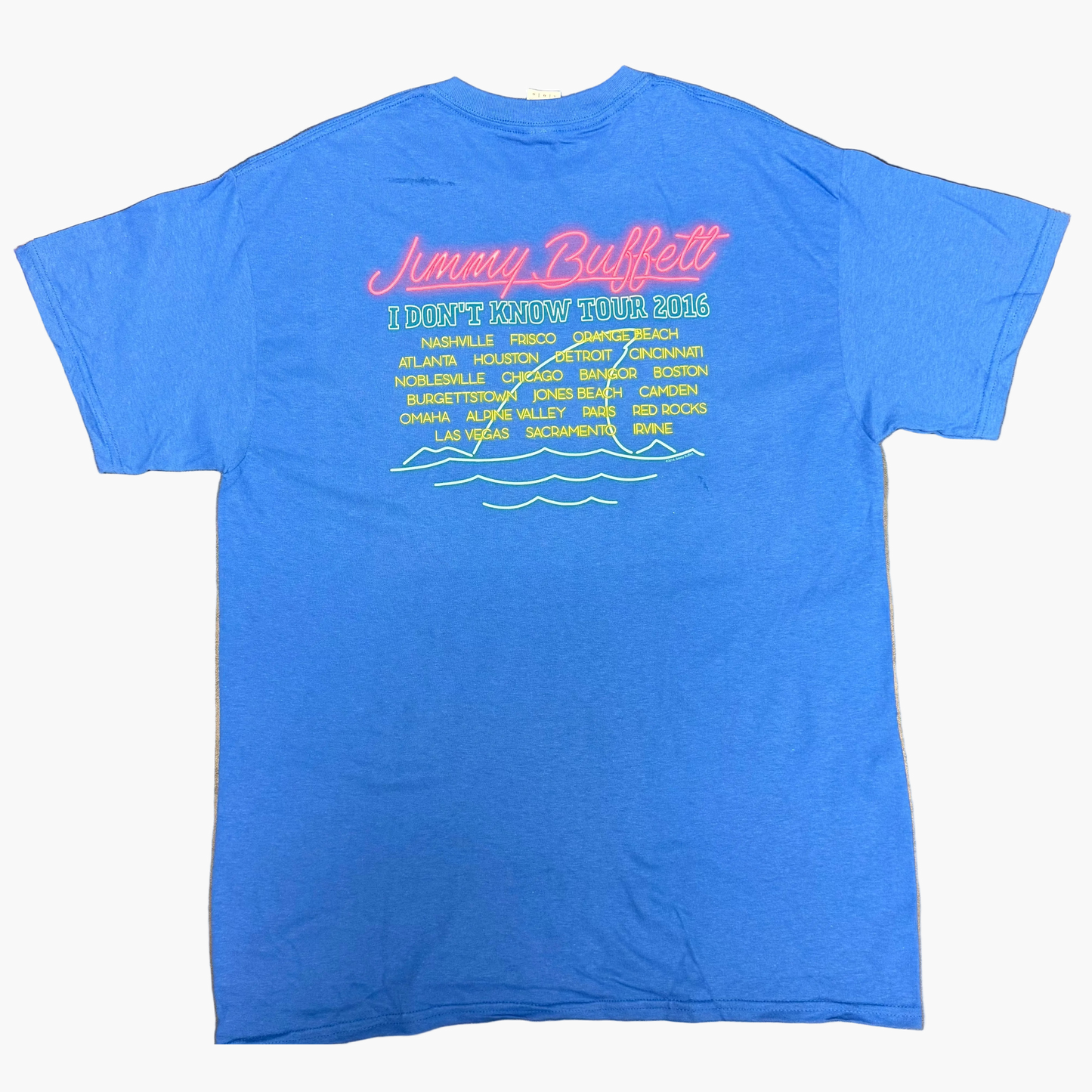 Back of a royal blue short sleeve Jimmy Buffett tee featuring pink “Jimmy Buffett” lettering above “I Don’t Know Tour 2016” text. A list of tour cities appears below in yellow and green, finished with a simple wave graphic at the bottom.