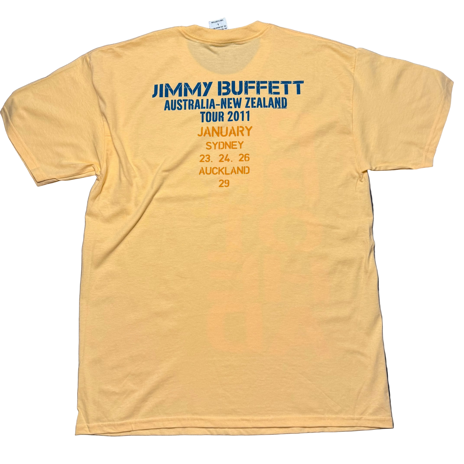 Back of a light yellow short sleeve Jimmy Buffett tee featuring blue “Jimmy Buffett Australia New Zealand Tour 2011” lettering above orange tour date text. The design lists January performances in Sydney on the 23rd, 24th, and 26th, and Auckland on the 29th.