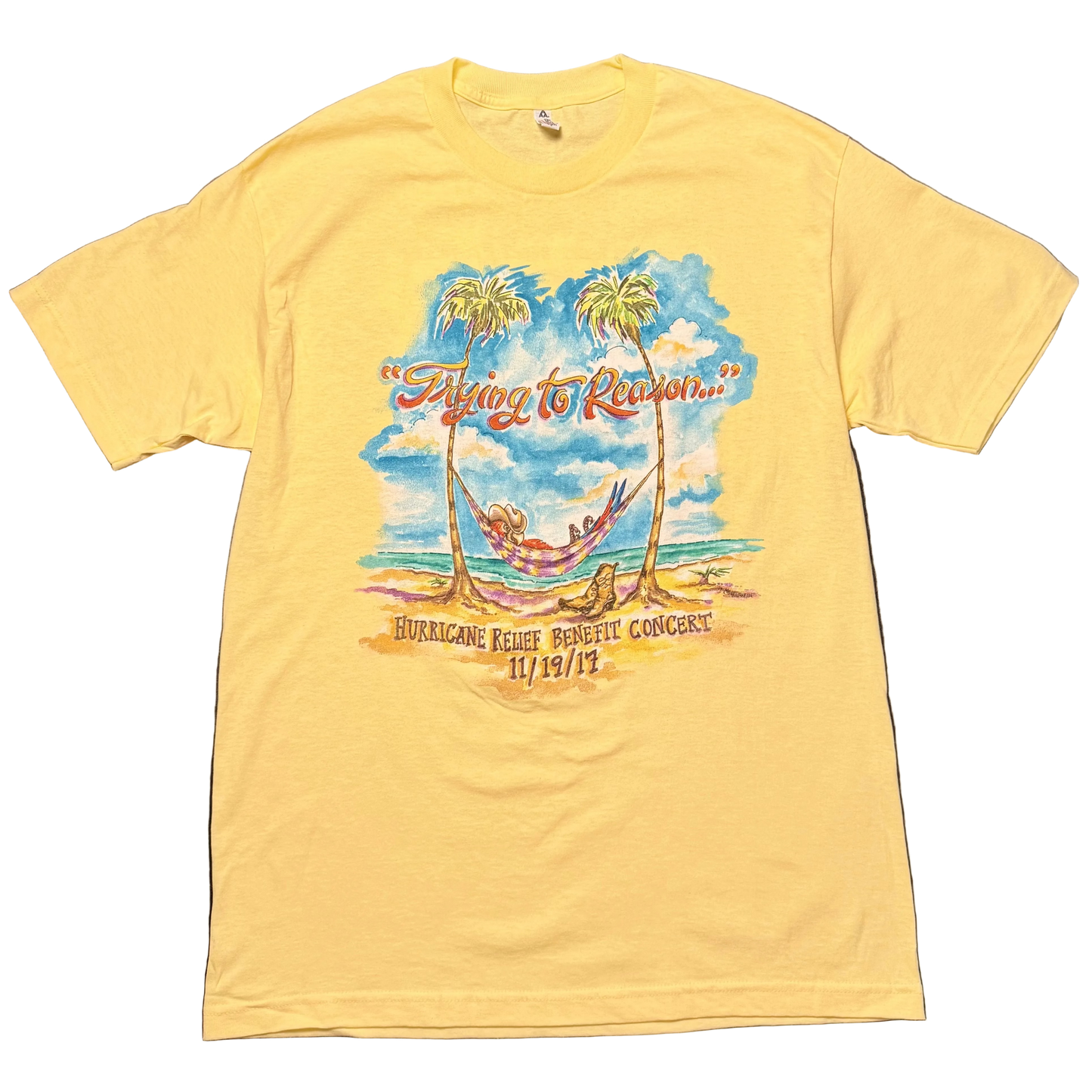 Light yellow short sleeve Jimmy Buffett tee featuring a tropical beach scene with a hammock strung between two palm trees beneath a blue sky. “Trying to Reason…” appears across the top, with “Hurricane Relief Benefit Concert 11/19/17” printed below.
