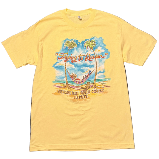 Light yellow short sleeve Jimmy Buffett tee featuring a tropical beach scene with a hammock strung between two palm trees beneath a blue sky. “Trying to Reason…” appears across the top, with “Hurricane Relief Benefit Concert 11/19/17” printed below.