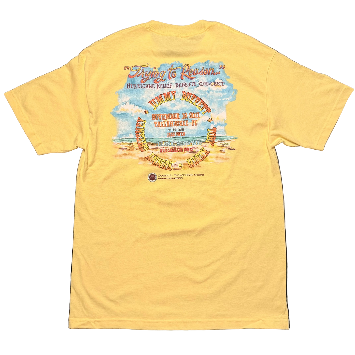 Back of a light yellow short sleeve Jimmy Buffett tee featuring “Trying to Reason…” and “Hurricane Relief Benefit Concert” above a beach scene. The design lists Jimmy Buffett, Kenny Chesney, Toby Keith, Jake Owen, the Coral Reefer Band, and Caroline Jones, with the November 19, 2017 Tallahassee, Florida event details and Donald L. Tucker Civic Center logo below.