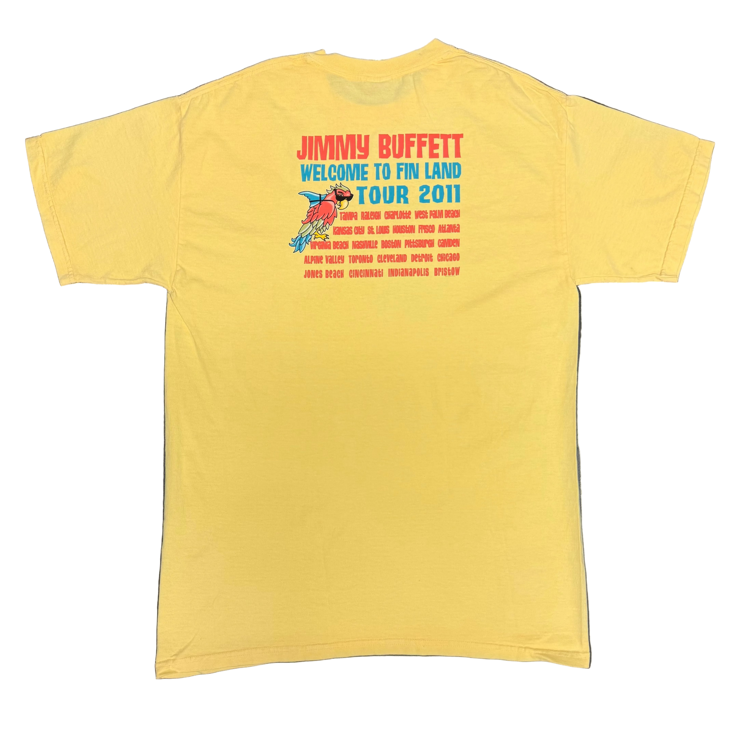 Back of a light yellow short sleeve Jimmy Buffett tee featuring large red “Jimmy Buffett” lettering above blue “Welcome to Fin Land Tour 2011” text. A smaller parrot with sunglasses and a shark fin appears beside a list of tour cities printed in red.