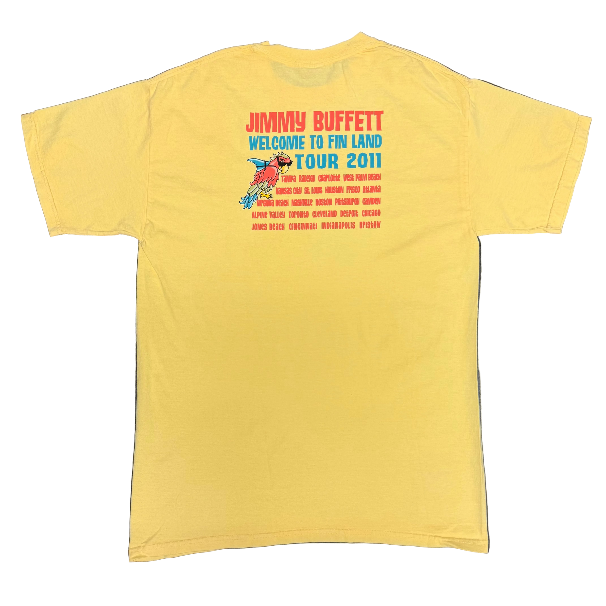 Back of a light yellow short sleeve Jimmy Buffett tee featuring large red “Jimmy Buffett” lettering above blue “Welcome to Fin Land Tour 2011” text. A smaller parrot with sunglasses and a shark fin appears beside a list of tour cities printed in red.